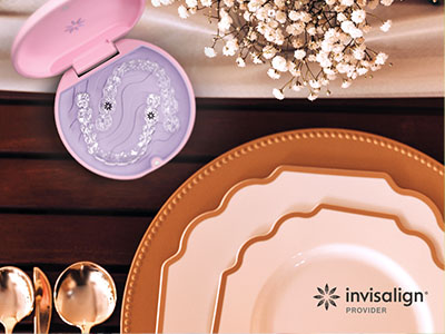 An advertisement image showcasing a set of tableware with a focus on a toothbrush-shaped container and an Invisalign aligner, placed on a dining table with a pink box and other accessories.