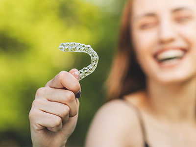 An image of a person holding up a clear dental retainer with a smile.