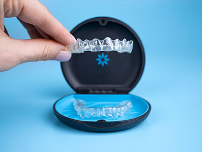 A person s hand holding a clear plastic tray with a blue and black dental retainer inside.